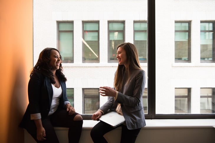 Two female co-workers stand by the window and chat
