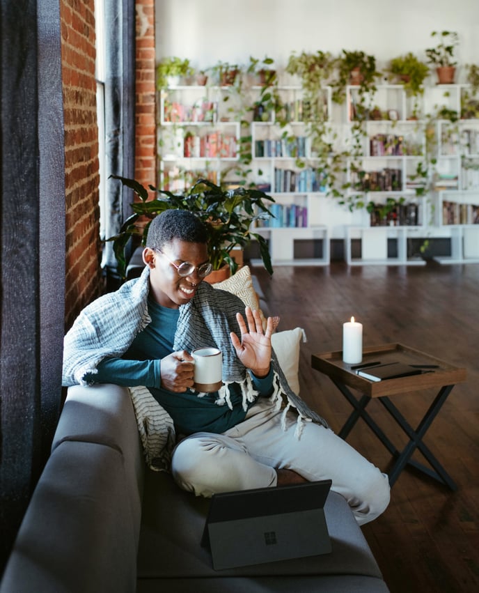 A person of color with a cup sitting on the couch attending an online meeting