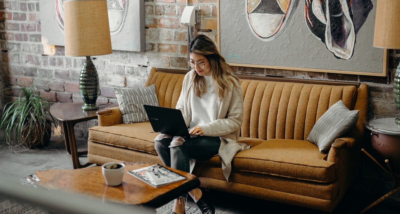 Woman sits on the couch typing on laptop