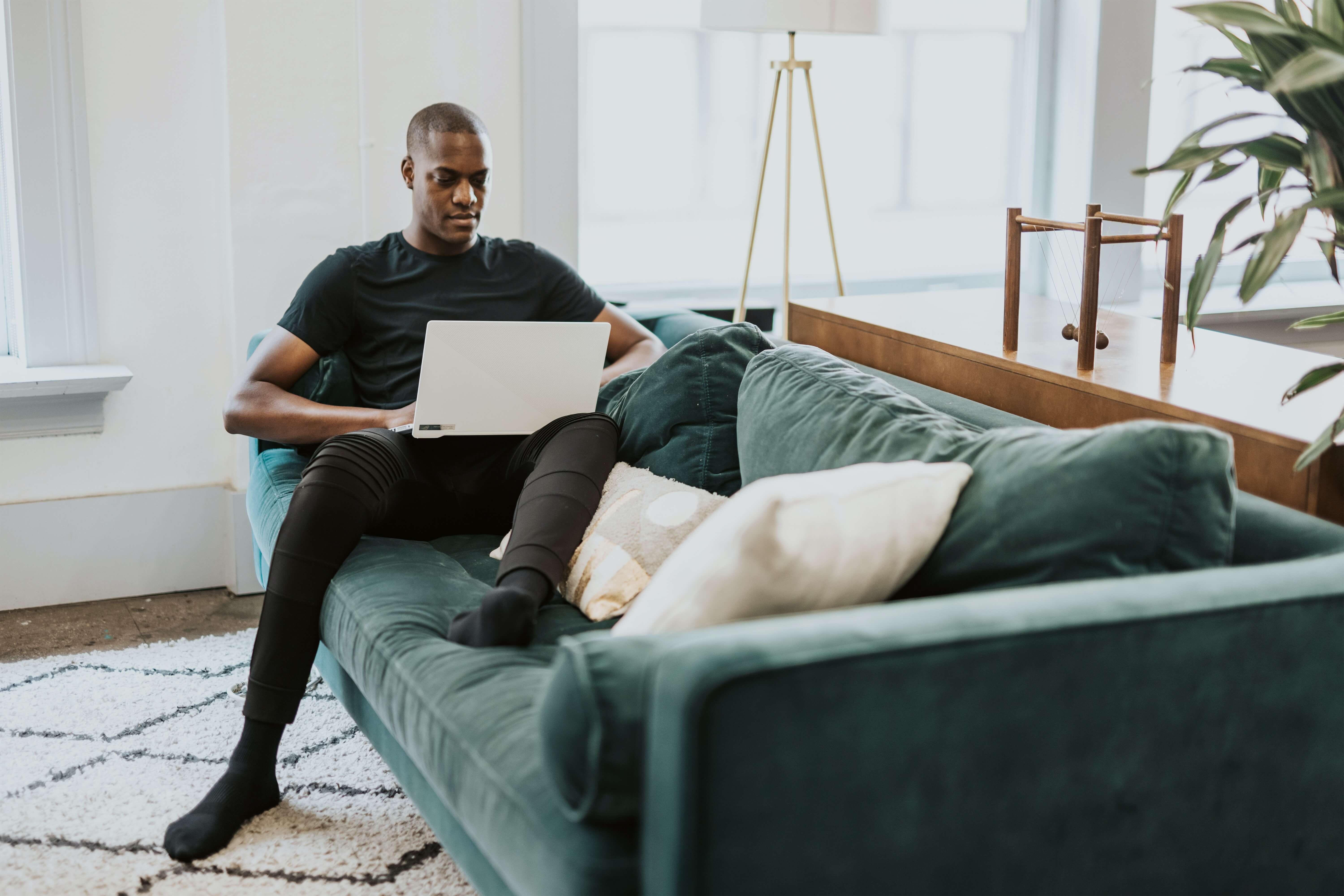 A man of color on the couch working on his computer